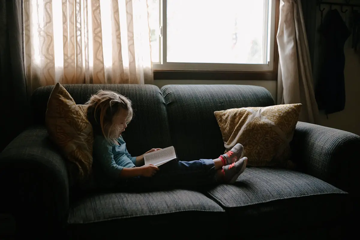 Little girl reading bible on couch